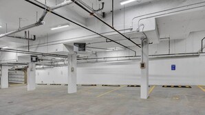 A spacious indoor parking area with concrete floors and white walls, featuring several pillars and a blue handicap parking sign. - Crescent Heights Hideout. (Calgary)