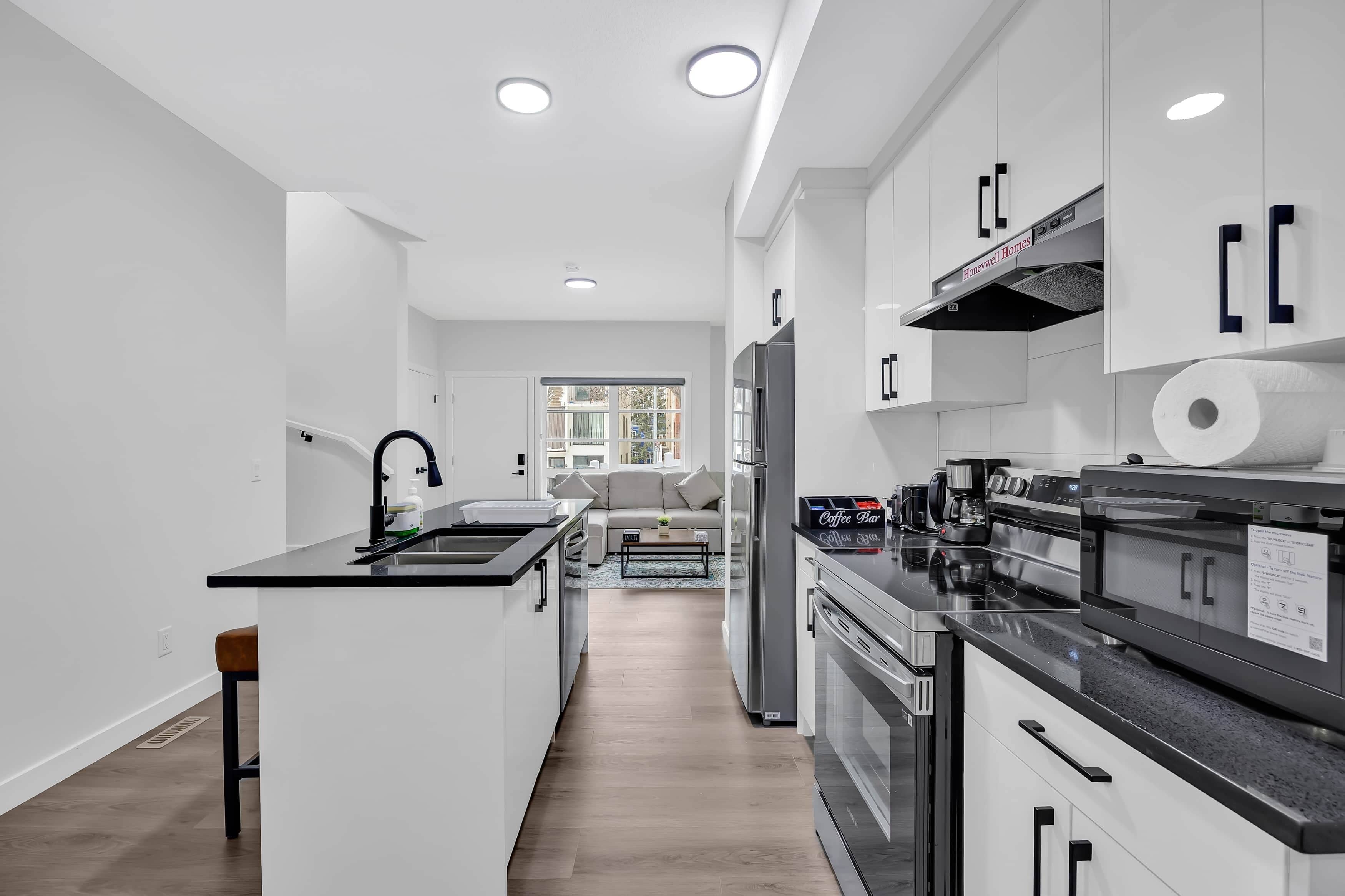 A modern kitchen with white cabinets, a black countertop, stainless steel appliances, and a central island.