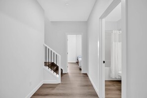 A hallway with a staircase, a door leading to a bathroom, and a bed in the distance. - Crescent Heights Oasis (Calgary)