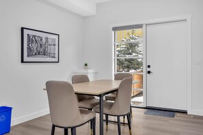A dining area with a table and chairs, a framed picture on the wall, a potted plant, and a sliding glass door leading to a balcony. - Crescent Heights Oasis (Calgary)