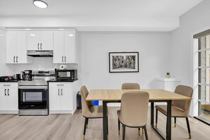 A modern kitchen with white cabinets, a built-in oven, and a dining area with a wooden table and four chairs. - Crescent Heights Oasis (Calgary)