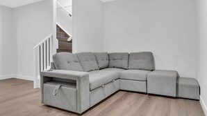 En grå hjørnesofa i et rum med trægulv og hvide vægge.