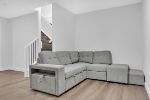 A grey sectional sofa in a room with wooden flooring and white walls. - Crescent Heights Oasis (Calgary)
