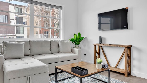 En moderne stue med en modulsofa, et sofabord, et fjernsyn ophængt på væggen og en potteplante.