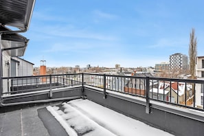 A rooftop with a metal railing, a snow-covered ground, and a view of surrounding buildings. - Crescent Heights Oasis (Calgary)