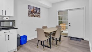 A modern kitchen with white cabinets, a microwave, a roll of paper towels, a blue recycling bin, and a dining table with chairs. - Modern Villa in the heart of Crescent Heights (Calgary)