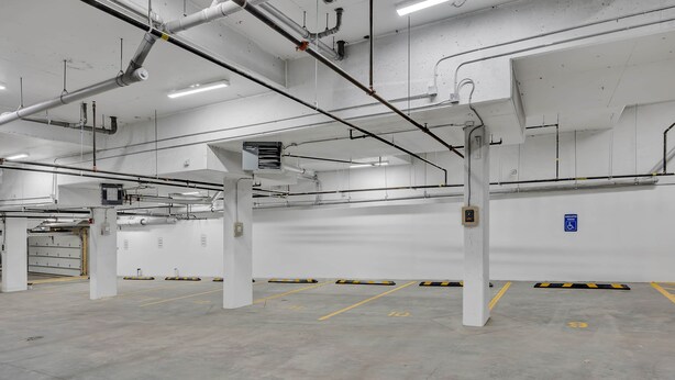A clean, empty parking garage with white walls, concrete floors, and visible structural elements like pipes and columns. - Modern Villa in the heart of Crescent Heights (Calgary)