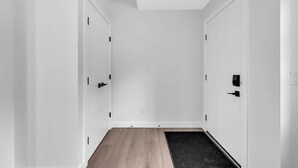 A hallway with white walls, a wooden floor, and two doors with black handles. - Modern Villa in the heart of Crescent Heights (Calgary)