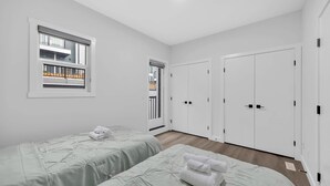 A bedroom with two beds, a window, a door, and a wardrobe. - Modern Villa in the heart of Crescent Heights (Calgary)