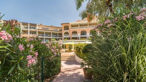 Un cortile alberato di un hotel, con un percorso centrale circondato da piante rigogliose e fiori rosa.