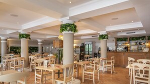 Un'ampia sala ristorante con numerosi tavoli e sedie, un'area bar e piante ornamentali.