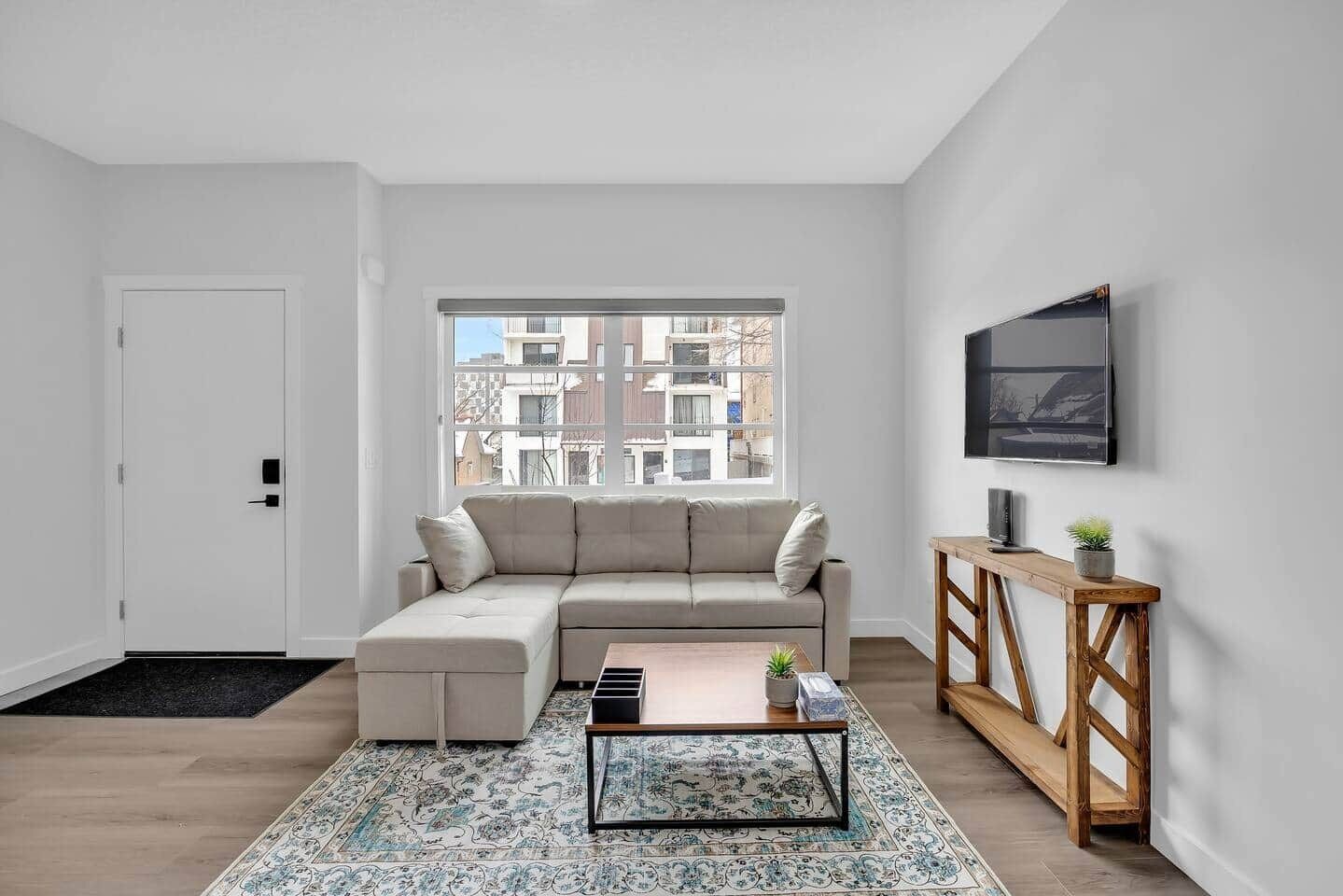 Ein modernes Wohnzimmer mit einem Ecksofa, einem Couchtisch, einem Fernseher auf einem Holzboden und einem großen Fenster mit Blick auf die Stadt.