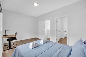 Une chambre d’hôtel avec un lit, un bureau, une chaise et une salle de bain visible à travers une porte ouverte.