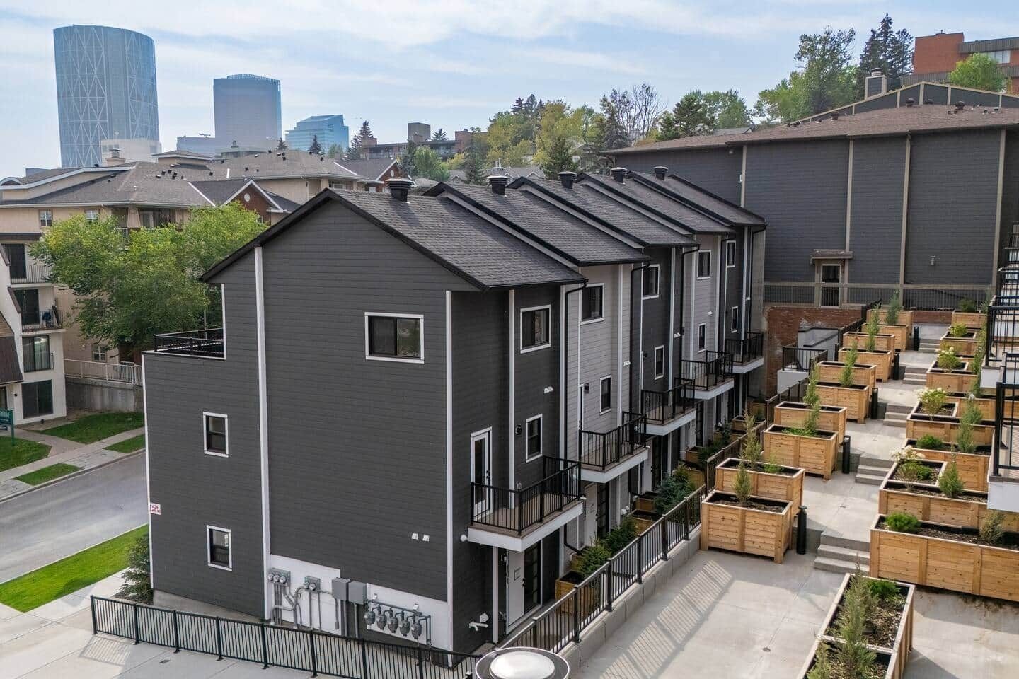 Um edifício residencial de vários andares com varandas, um jardim no terraço e vista para a cidade.