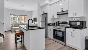 A modern kitchen with white cabinets, stainless steel appliances, and a central island with stools. - Work away from home! Crescent Heights. (Calgary)