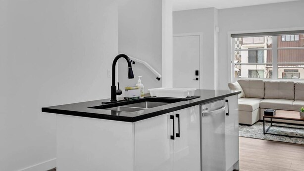 A modern kitchen with a black countertop, white cabinets, and a black faucet. - Work away from home! Crescent Heights. (Calgary)