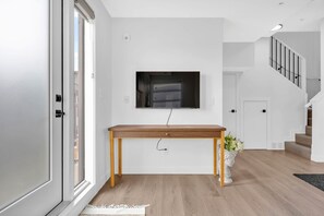 A modern living room with a wooden console table, a mounted TV, and a staircase leading to an upper floor. - Urban Cozy Loft ! 5 min to Downtown (Calgary)