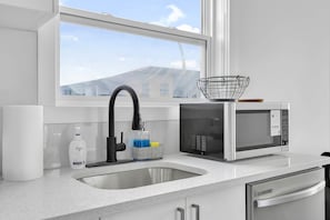 A kitchen with a white countertop, a stainless steel sink, a black faucet, a microwave, and a window above the sink. - Urban Cozy Loft ! 5 min to Downtown (Calgary)