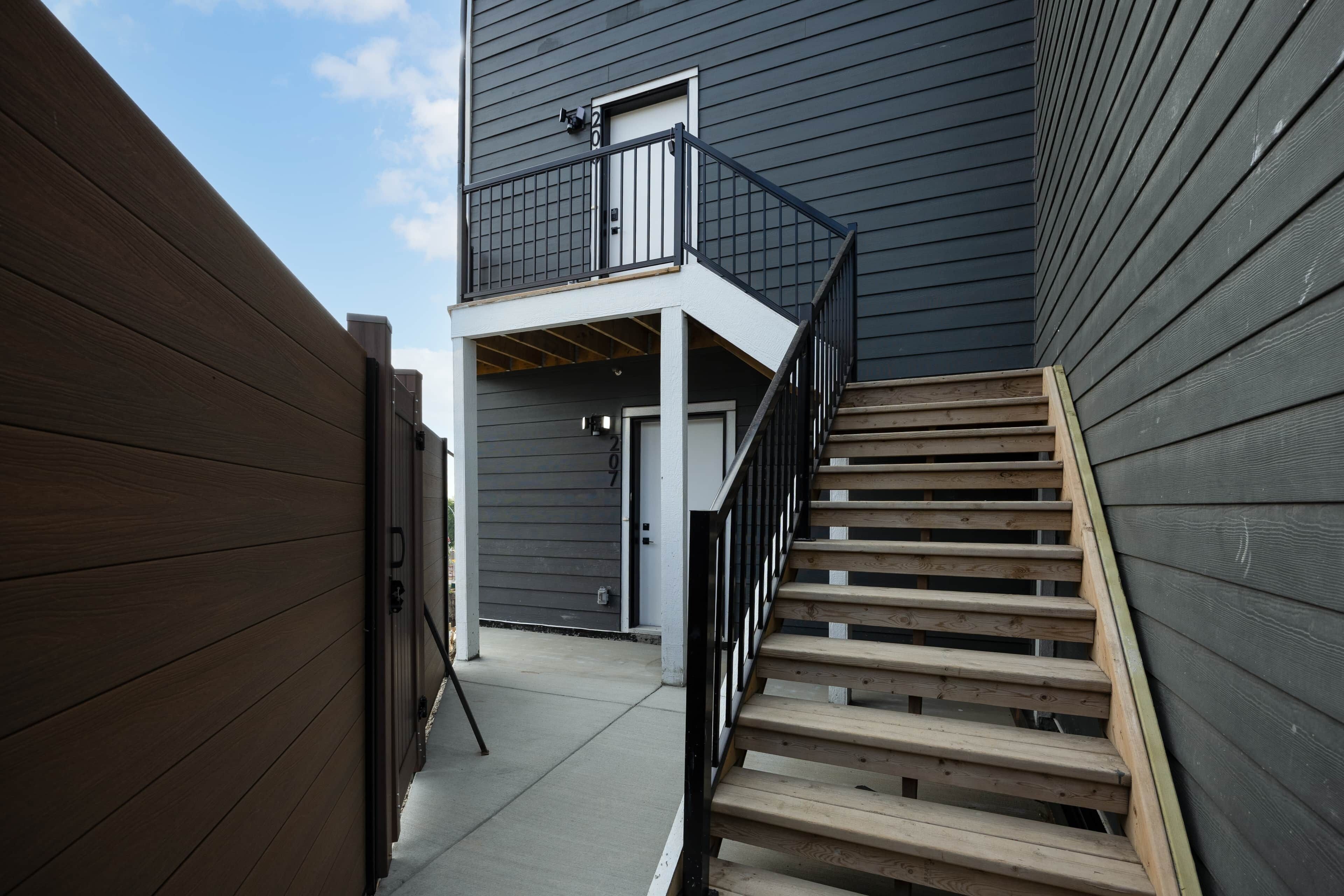 Un edificio residencial con fachada de madera, un balcón y una escalera que conduce a la entrada.