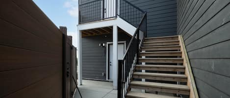 Un edificio residencial con fachada de madera, un balcón y una escalera que conduce a la entrada.
