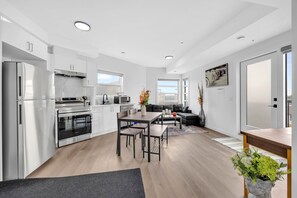 Eine moderne Küche mit weißen Schränken, einem Edelstahlkühlschrank und einem Backofen. Es gibt eine Essecke mit Tisch und Stühlen.