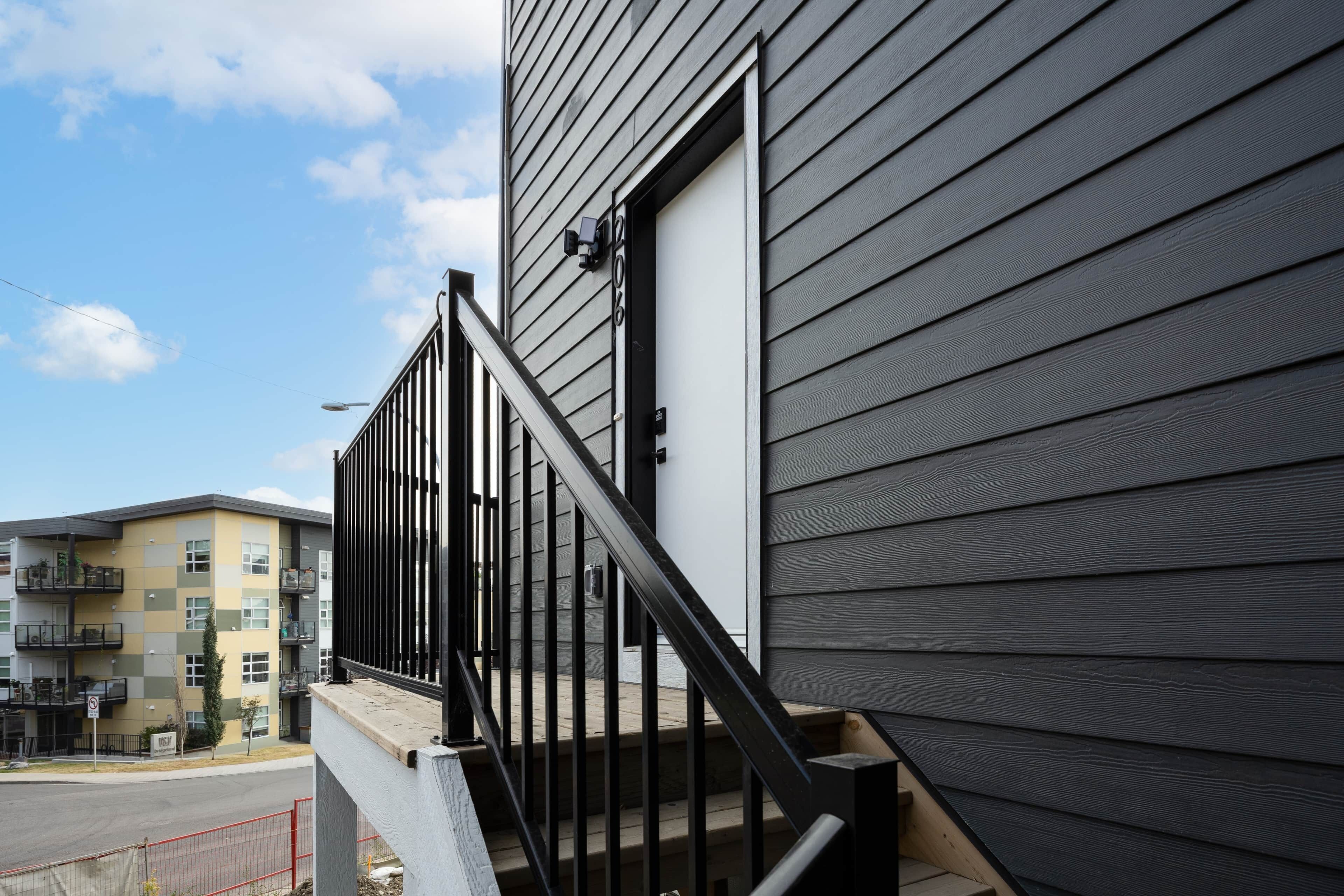 A residential building with a grey exterior, a black metal staircase, and a visible door.