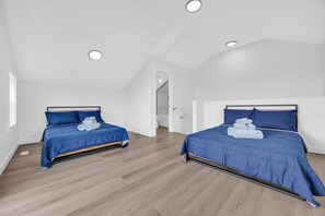 A bedroom with two beds, wooden flooring, white walls, and a sloped ceiling with recessed lighting. - Urban Cozy Loft ! 5 min to Downtown (Calgary)