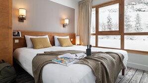 Ein Hotelzimmer mit einem großen Bett, zwei Nachttischlampen, einem Fenster mit Blick auf verschneite Bäume und einem hölzernen Kopfteil.