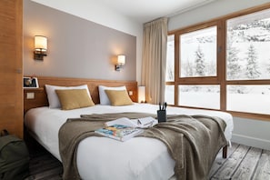 Ein Hotelzimmer mit einem großen Bett, zwei Nachttischlampen, einem Fenster mit Blick auf verschneite Bäume und einem hölzernen Kopfteil.