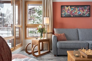 Ein gemütliches Wohnzimmer mit einem grauen Sofa, einem Holztisch mit Blumenvase und einem Schachbrett.