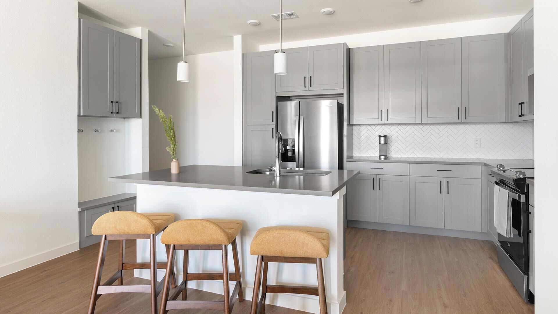 A modern kitchen with grey cabinets, a stainless steel refrigerator, and a central island with bar stools.