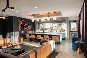 Ein modernes Wohnzimmer mit einer Couch, Sesseln, einem Couchtisch, einer Bar mit Barhocker und einem großen Fenster mit Blick auf die Stadt.