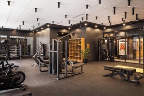 Ein Fitnessraum mit unterschiedlichen Trainingsgeräten, einer Bank und einer Wanduhr.
