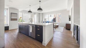 A modern kitchen with a central island, dark cabinetry, and pendant lighting. - Landing | Stylish 2BD, Rooftop Lounge, Gym (Denver)