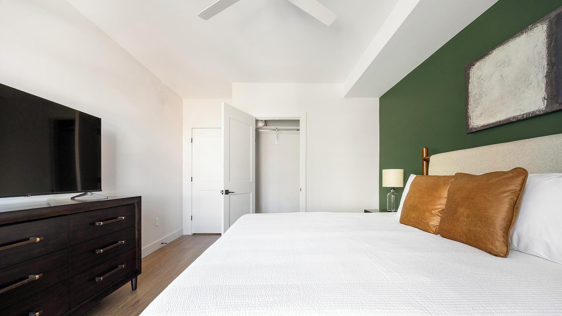 A bedroom with a bed, a dresser, a television, and a door leading to a closet.