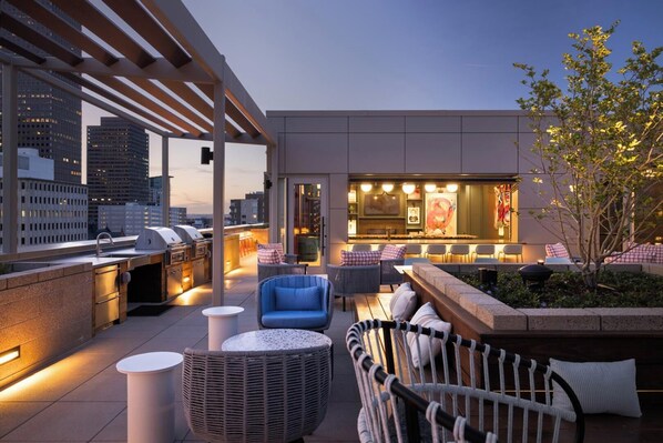 A rooftop terrace with outdoor seating, a bar area, and a grill. - Landing | Modern 2BD, Rooftop Lounge, Gym (Denver)