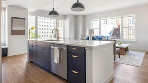 A modern kitchen with a central island, dark cabinetry, and pendant lighting. - Landing | Stylish 2BD, Rooftop Lounge, Gym (Denver)