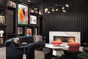 A modern living room with a dark-colored sofa, a fireplace, and a bookshelf with various framed artworks. - Landing | Stunning 2BD, Rooftop Lounge, Gym (Denver)