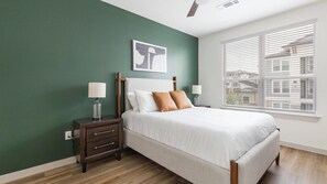 Ein Schlafzimmer mit einem Bett, Nachttischen, einem Fenster mit Jalousien und Blick auf die Stadt.