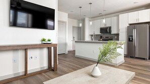 Eine moderne Küche mit Flachbildfernseher, Holztisch und einer Vase mit Grünpflanzen.