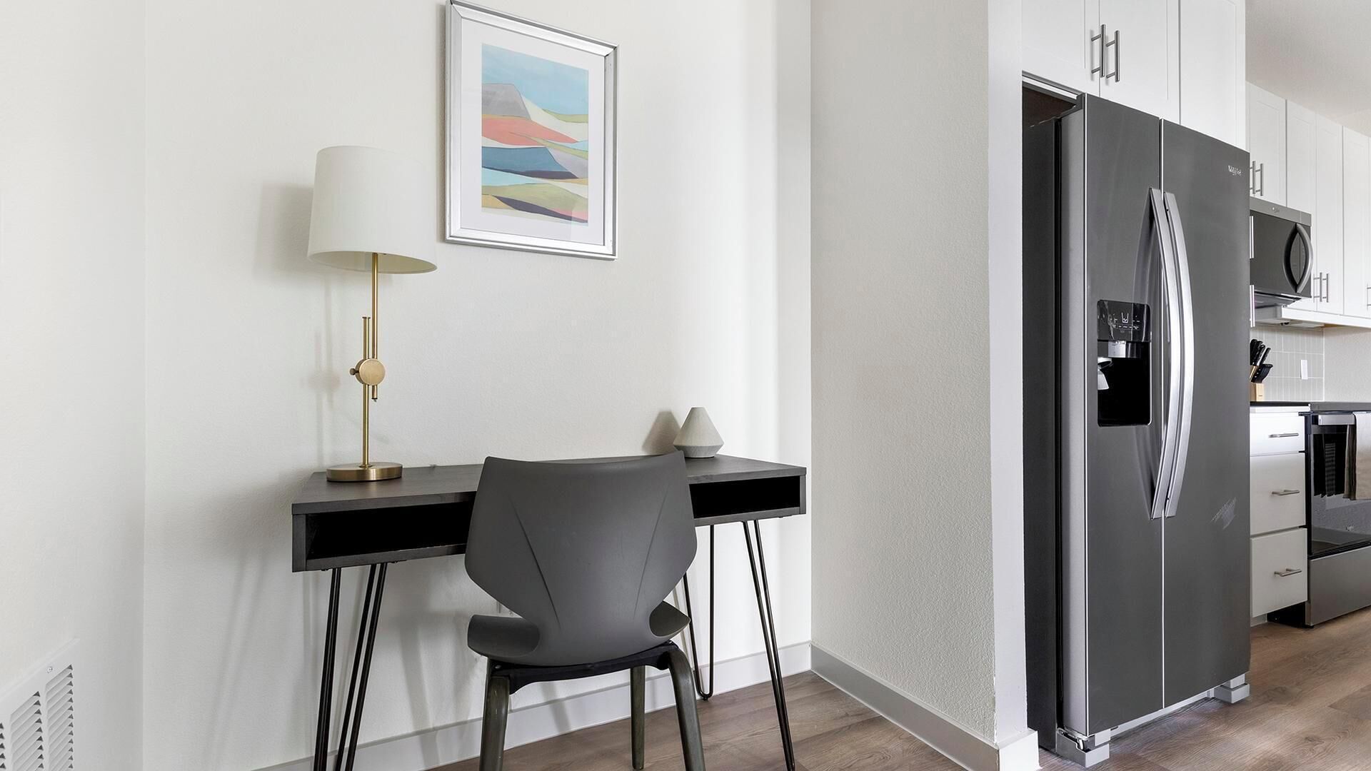 A modern kitchen with a black refrigerator, a dining table with a chair, and a framed picture on the wall.