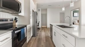 Une cuisine moderne dotée d’appareils électroménagers en acier inoxydable, de meubles blancs et d’un plancher en bois.