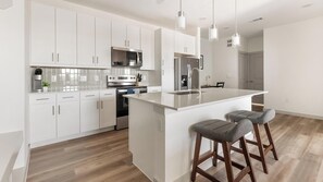 A modern kitchen with white cabinetry, stainless steel appliances, and a central island with bar stools. - Landing | Amazing 1BD in Northwest Side (San Antonio)