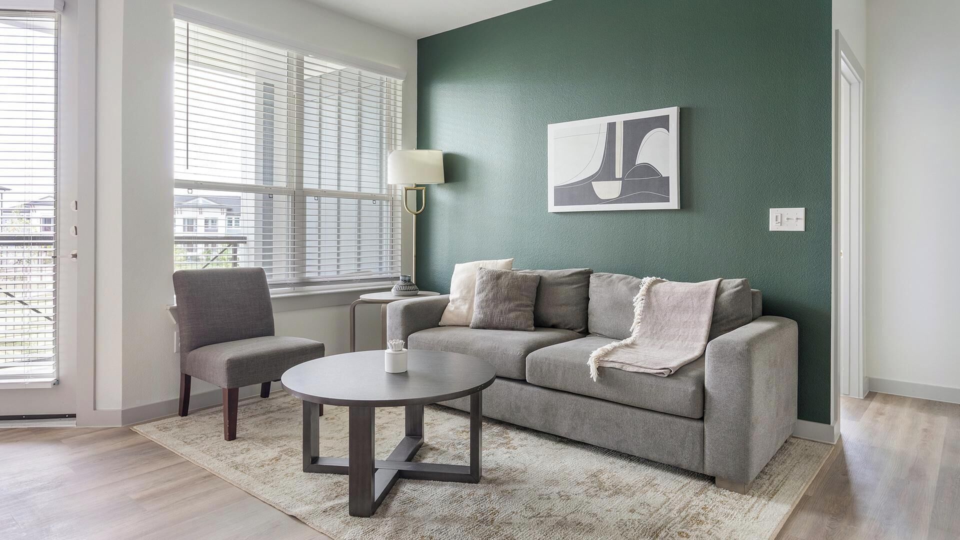 Ein Wohnzimmer mit einem grauen Sofa, einem runden Couchtisch, einem grauen Sessel und einem Bild an der Wand.