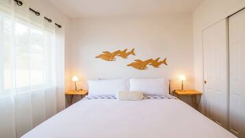 A bedroom with a large bed, two bedside tables with lamps, sheer curtains, and wooden wall art of fish.