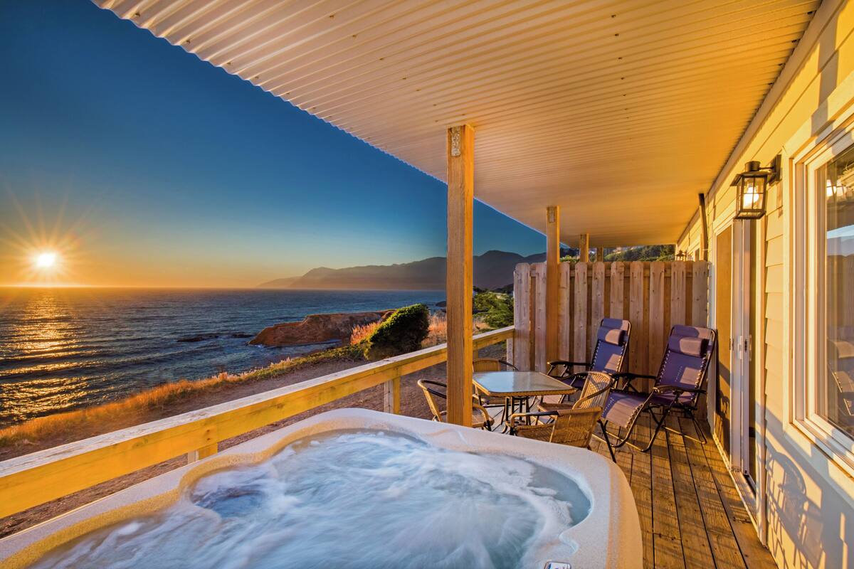 Un jacuzzi en una terraza de madera con vista al océano al atardecer.
