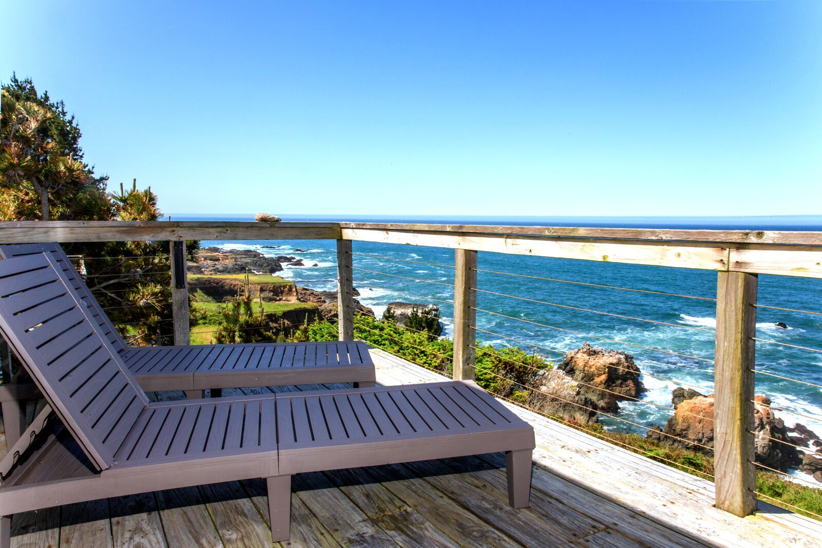 A wooden deck with two lounge chairs overlooking a rocky coastline and ocean.