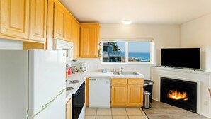 Una cocina con armarios de madera, un refrigerador blanco, una estufa, un lavavajillas, un fregadero, un ventanal con vista al océano y una chimenea.