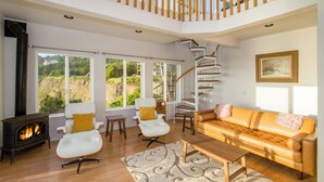 Amplia sala de estar con piso de madera, un sofá, dos sillones, una mesa de centro, una chimenea y una escalera en espiral.