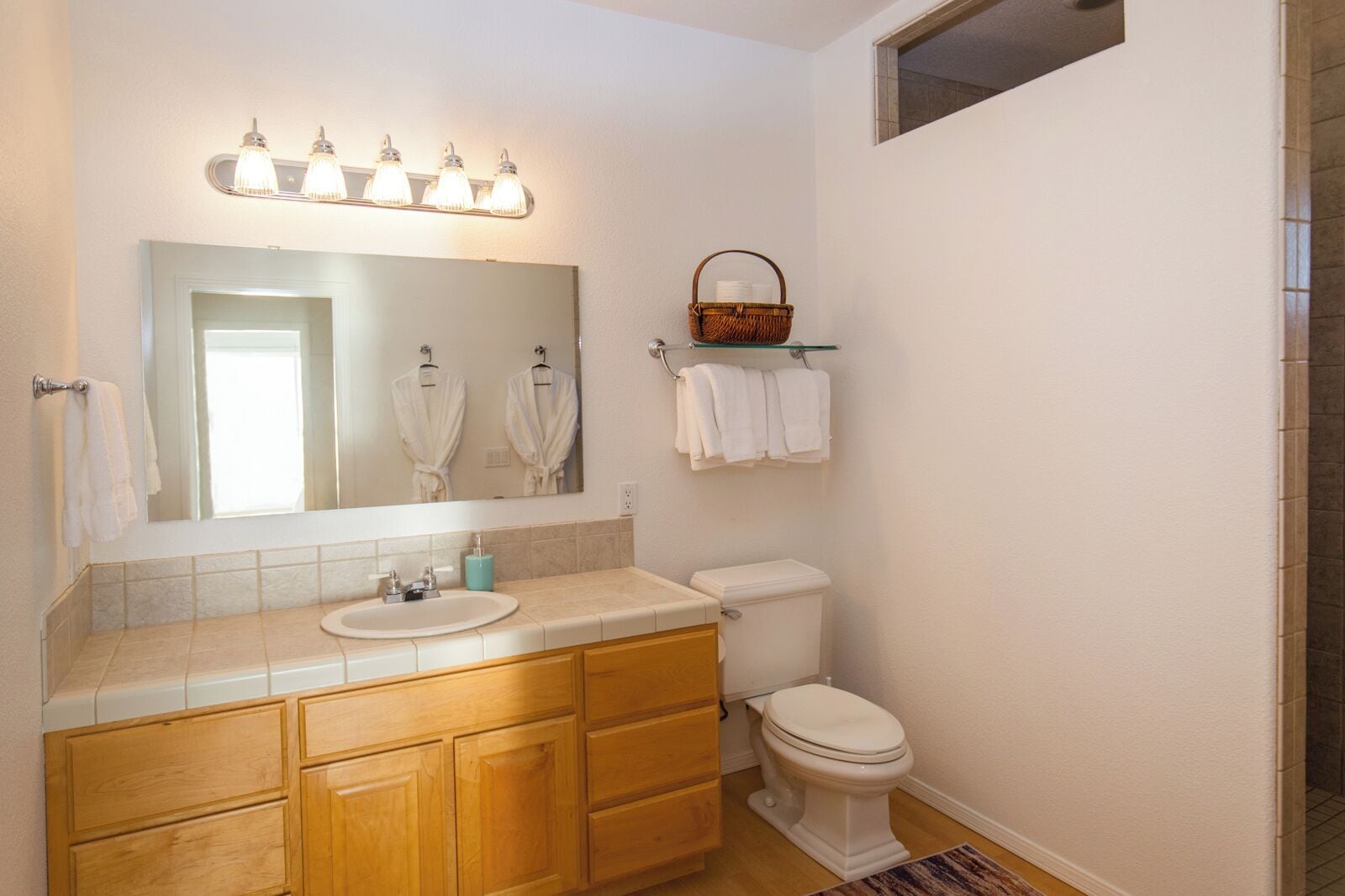 A bathroom with a sink, mirror, vanity, toilet, and a window.